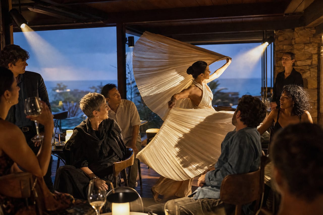 Conceptual imagery: a dancer sweeps a pleated fabric fan through an intimate terrace gathering as guests turn toward the shared moment.
